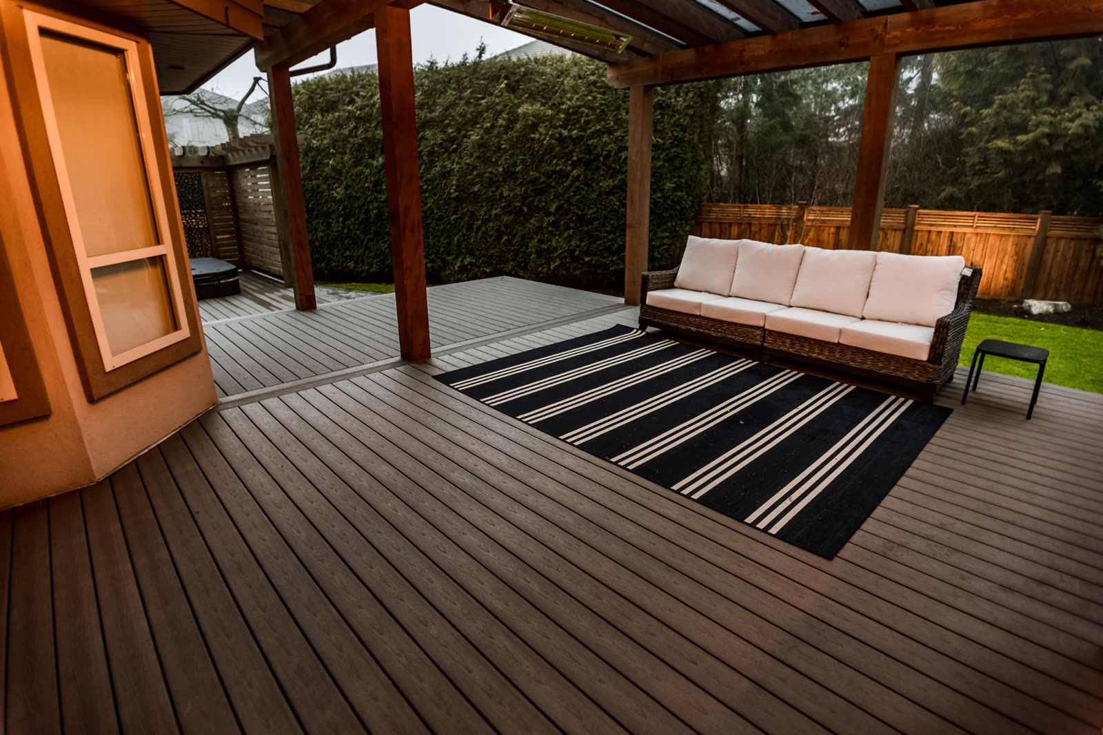 Covered composite deck with wicker sofa, striped outdoor rug, and timber posts framing a Fraser Valley backyard