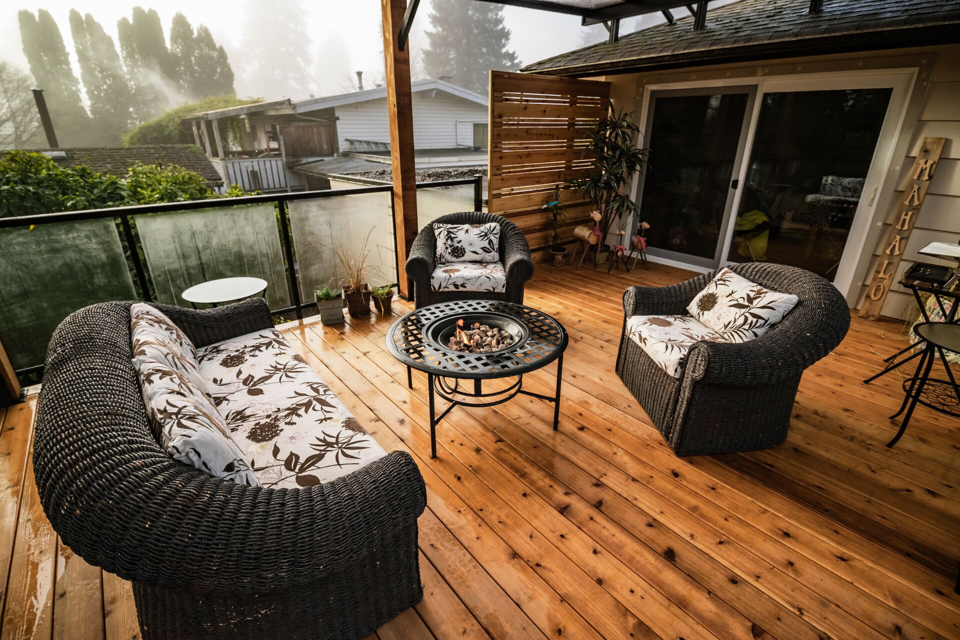 Cedar deck at dawn with wicker furniture, firepit table, and covered patio overlooking a misty Fraser Valley backyard