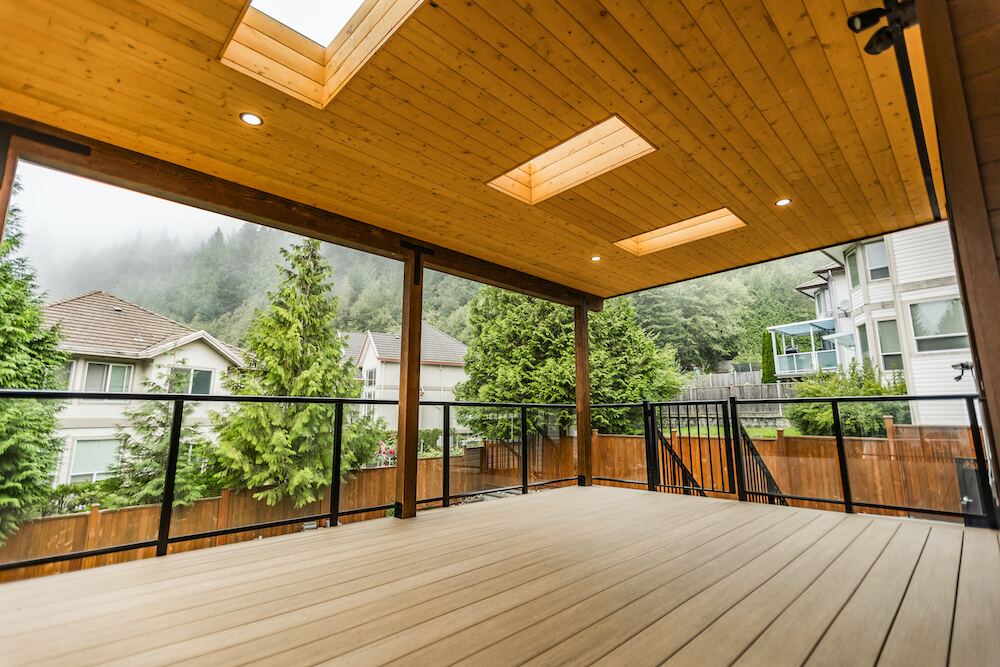 Covered composite deck with cedar tongue-and-groove ceiling and glass railings overlooking a forested mountainside