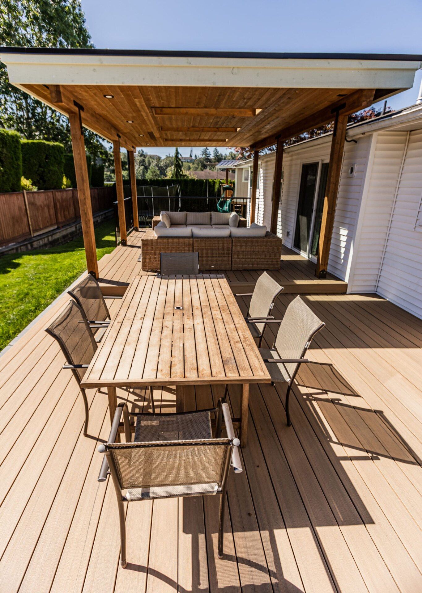 Sunlit two-tone composite deck with dining set and lounge seating under a cedar patio cover