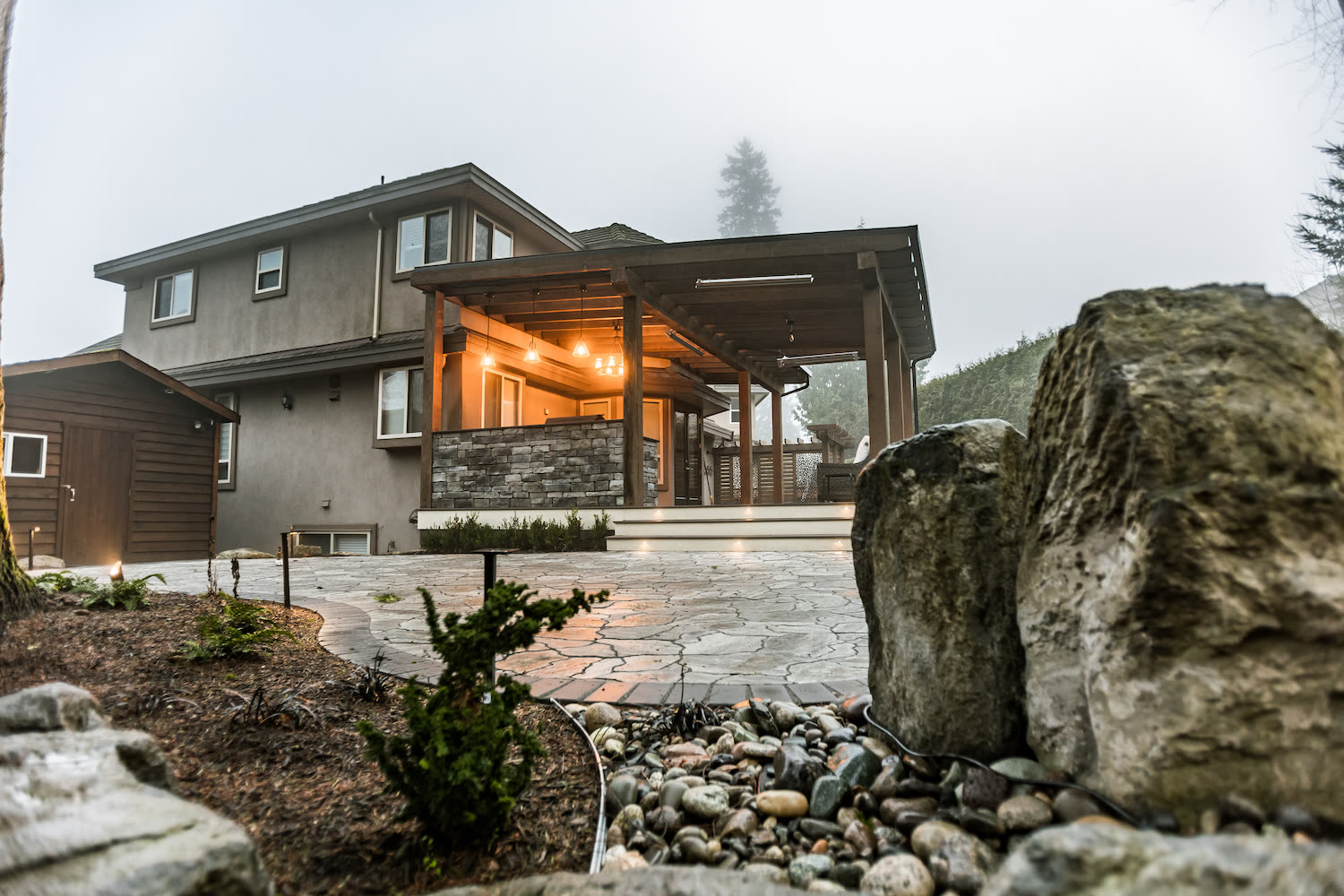 Custom patio cover with stone accents and landscape lighting at dusk