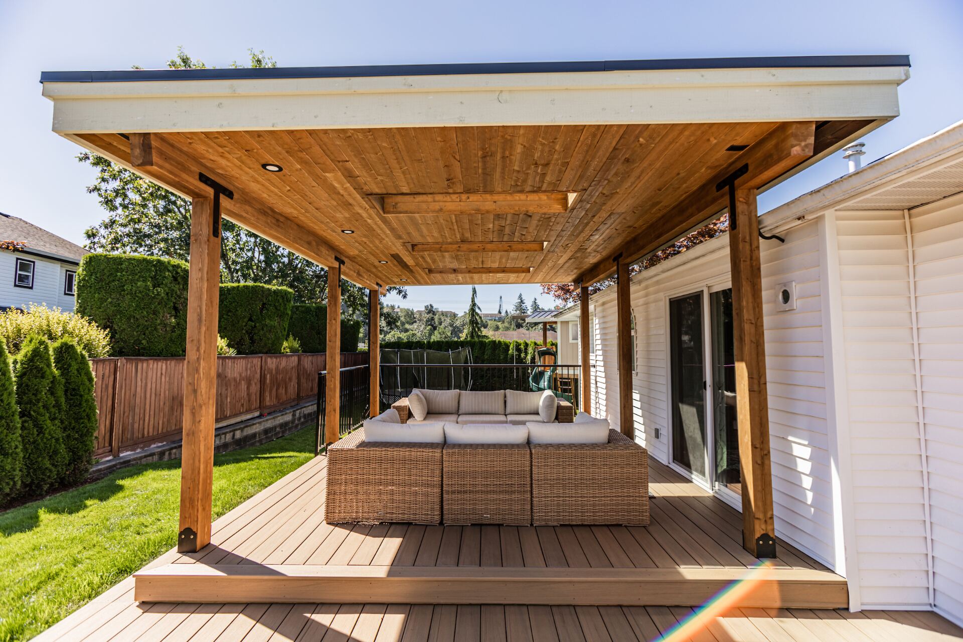 Custom flat-roof cedar patio cover with recessed lighting and exposed beams over a composite deck and outdoor lounge