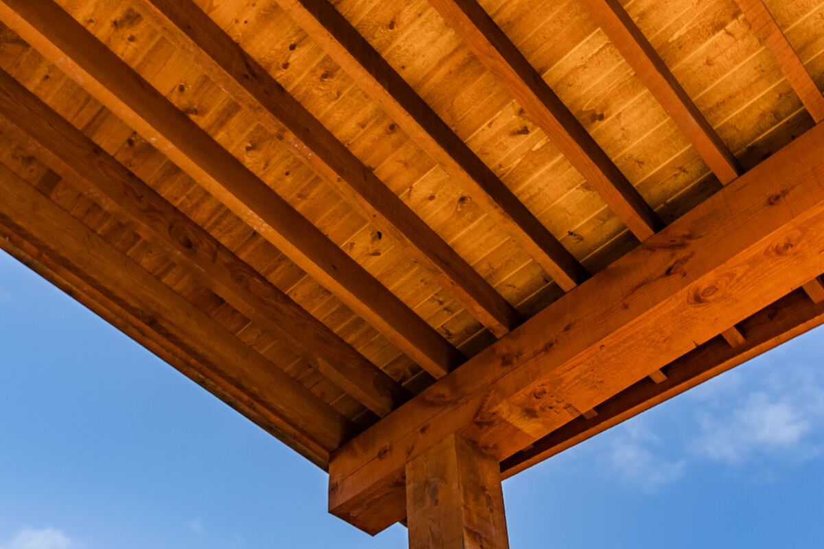 Detail of a stained cedar patio cover beam and tongue-and-groove underside against a clear blue sky
