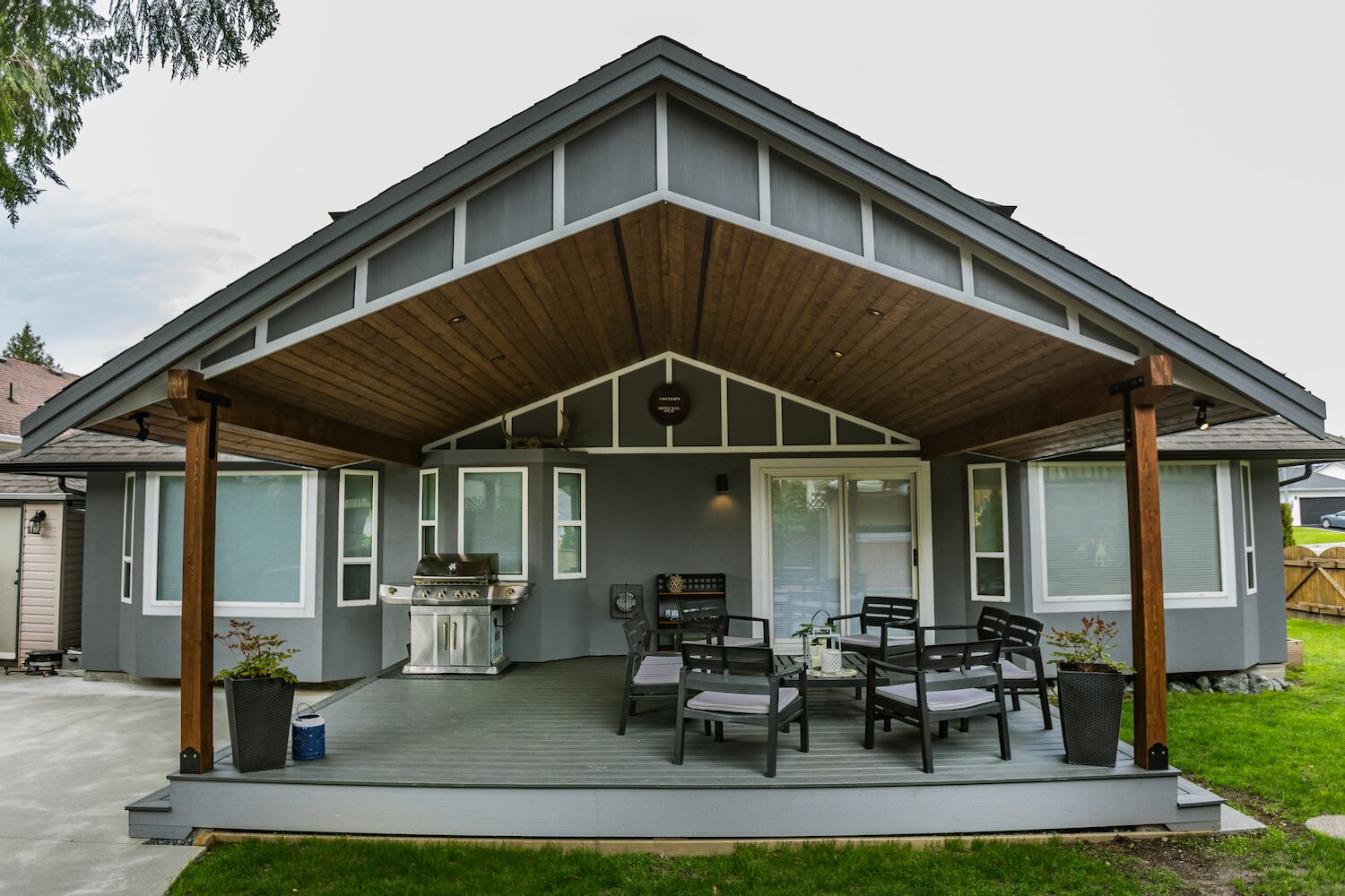 Custom gabled patio cover with cedar tongue-and-groove ceiling, exposed beams, and recessed lighting over a covered grey composite deck