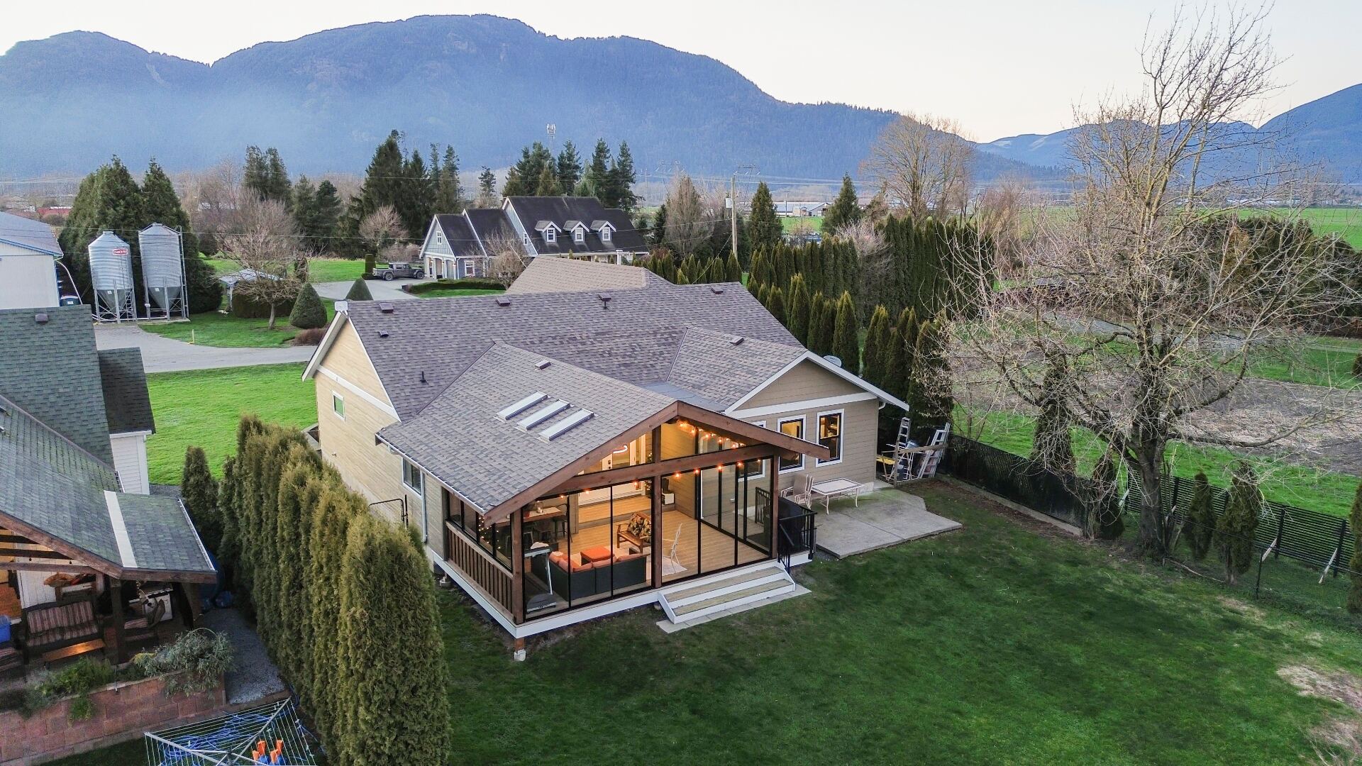 Aerial view of a custom Fine Line sunroom addition with vaulted timber roof and floor-to-ceiling glass, set against the Fraser Valley mountains